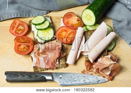 Snack with brown bread with cucumber tomatoes. Mortadelle and ham garnishes on a wooden board