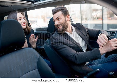 Businesswoman on the backseat with elegant man driving a car in the city. Worried about a delay to an important meeting