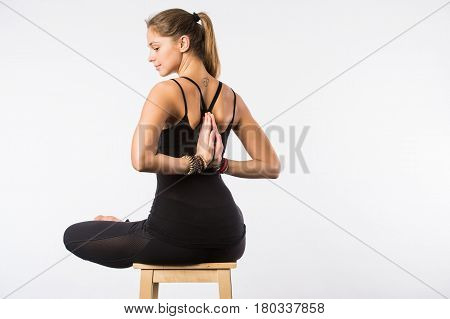Feel relaxed. Young pleasant woman sitting in lotus pose on chair with closed eyes and putting her palms together