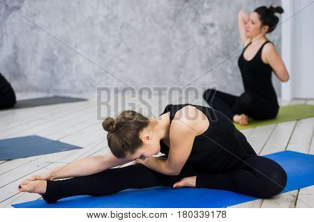 Shot of young women warming up before yoga session. Young people sitting on exercise mat in yoga class