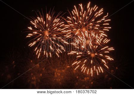 Three colorful bursts of red/white fireworks fill the center of the frame at the International Fireworks Festival at the Old Port of Montreal, Quebec, at night in July