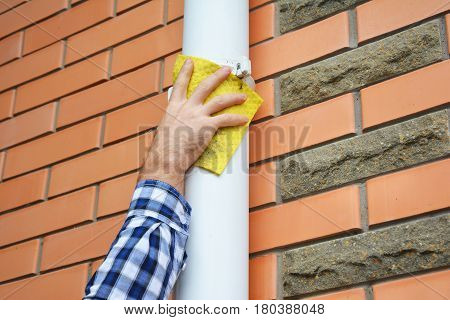 Man cleaning white pvc rain gutter system downspout pipeline. Cleaning White Gutters. Guttering.