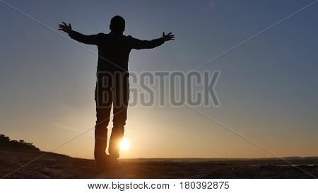 freedom. Man stands on a cliff sunset silhouette hand in sides lifestyle