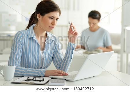 Portrait of a young female office worker, using laptop