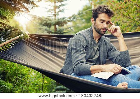 Man relaxing on hammock with book sun down