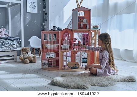 Feeling playful. Cute little girl playing with a dollhouse while sitting on the floor in bedroom