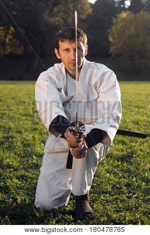 Ninja in white kimono with sword is practicing martial arts outdoors.