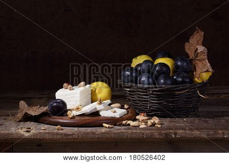 still life with cheese quince nuts and ripe plums in a wicker basket