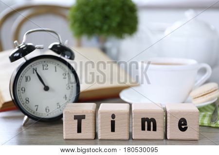 Retro alarm clock showing five minutes to eleven and wooden cubes with word TIME on lunch table