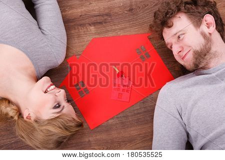 Housing marriage family security future finances mortgage concept. Just married lying on floor. Young man and woman next to home symbol with keyring.