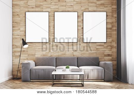 Front view of a living room with light wooden walls a long sofa and three framed vertical posters hanging above it. 3d rendering mock up
