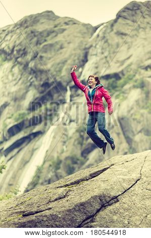 Happy woman jumping on rock in grey mountains enjoying traveling and adventure.
