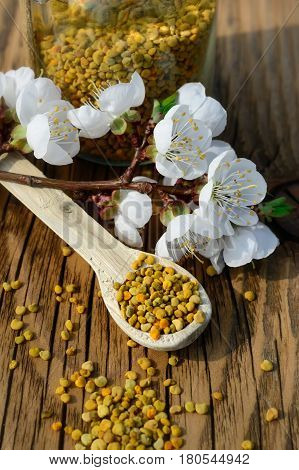 Grains of bee pollen in jar and wooden spoon on wooden table with decoration flowers. Apitherapy. Bee products