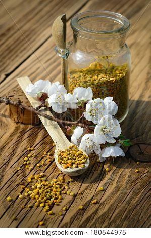 Grains of bee pollen in jar and wooden spoon on wooden table with decoration flowers. Apitherapy. Bee products