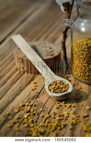 Grains of bee pollen in jar and wooden spoon on wooden table with decoration flowers. Apitherapy. Bee products