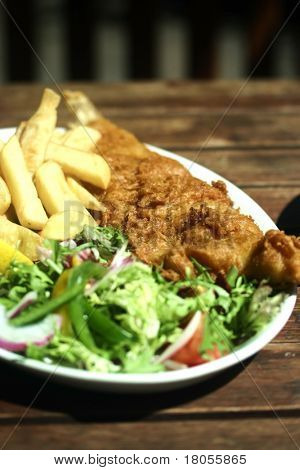 En plade af voldsramte fish and chips med frisk grøn salat på træbord