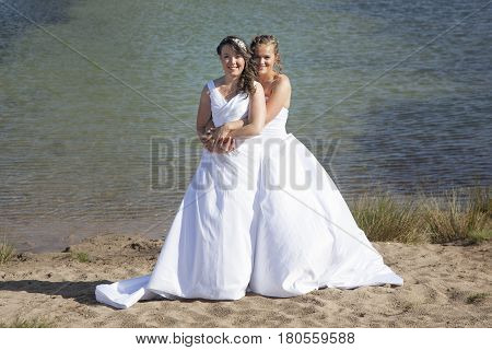 just married happy lesbian couple in white dress embrace near small lake and forest on sunny day