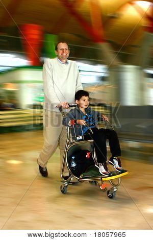 Un homme pousse son jeune fils sur le chariot de bagages vers la porte d'embarquement à l'aéroport, montrant 