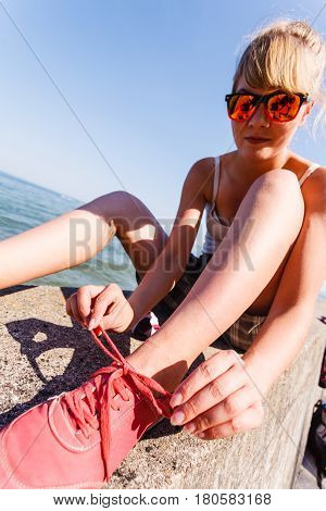 Outdoor relax holidays nature concept. Young girl tying shoelace. Lady sunbathing on coast making a knot.