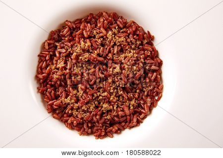 Red wild rice with sesame gomasio seasoning in a white plate over wooden board