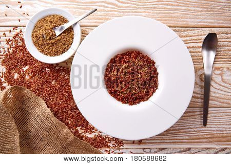 Red wild rice with sesame gomasio seasoning in a white plate over wooden board