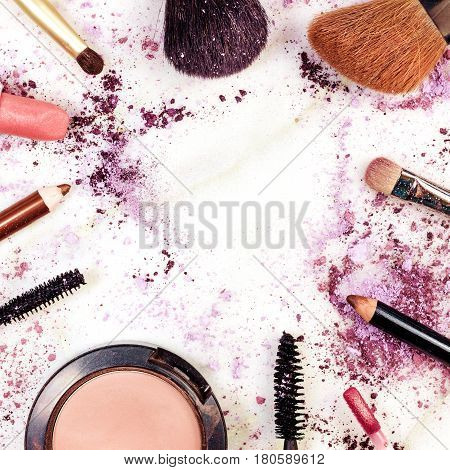 Makeup brushes, pencil, lipstick and other objects, forming a frame on a light background, with crushed powder and copy space. A squarel template for a makeup artist's business card or flyer design