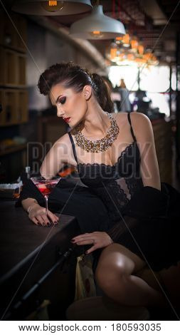 Sensual girl with long legs and high heels sitting on the chair in bar  drinking .Handsome girl wearing beautiful body and high heels in indoor scene.Fashion model with long sexy legs drink cocktail.