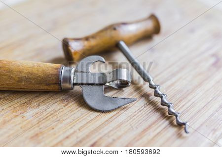 Vintage beer bottle opener and corkscrew with wooden worn handles of pleasant light brown color lying on a wooden table.Bar stuff concept