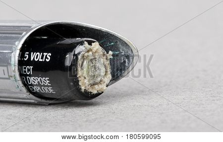 damaged alcaline battery against gray background, closeup