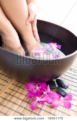 Donna ammollo i piedi in una ciotola di acqua profumata floreale in spa