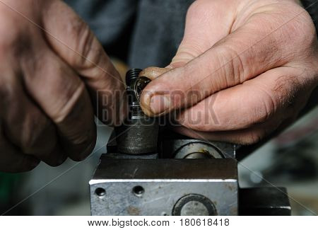 Mechanics repairing a diesel injector. Mans hands disassemble a injector pinched in a vise.
