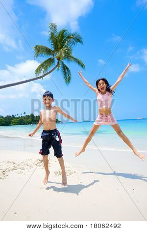 Bruder und Schwester hoch springen, beim haben des Spaßes am Sandstrand