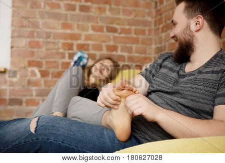 Man is massaging woman's foot, in home.
