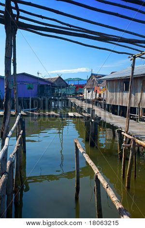 Passerella in legno che conduce a zinco e tetto di paglia case del villaggio di un'acqua di Tuaran, Sabah Malay