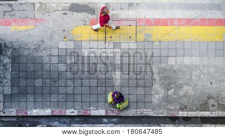 On street walk in top view man and woman with shopping bags stand on square block pedestrian walk way with yellow and red line for guide blind people walk (aerial city street view)