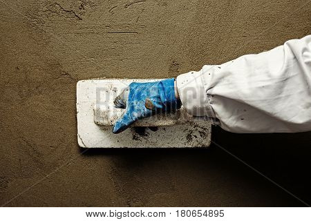 Worker working manual with wall plastering tools inside a house.
