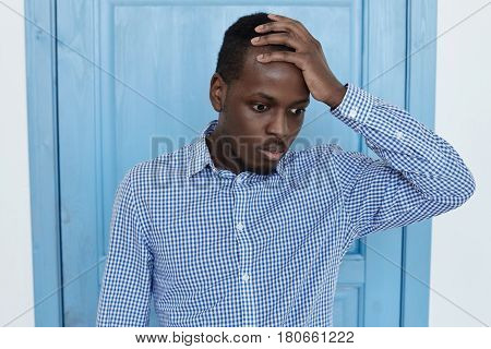 Young african american man holding his hand with quilty face. Portrait of office worker who forget failed something very important or made a big mistake. Negative human emotions and expressions concept.