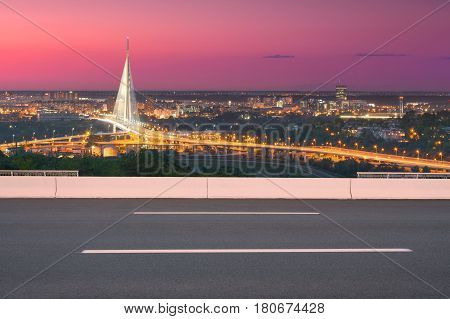 Side view on highway and the city in background shiny new bridge as well as modern access roads at idyllic purple sunset.