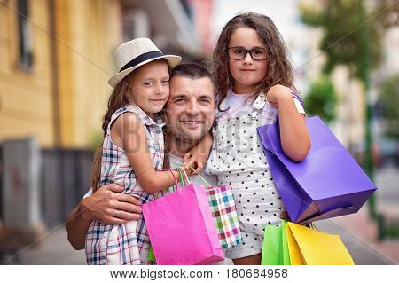 Happy daughters hugging father with shopping bags