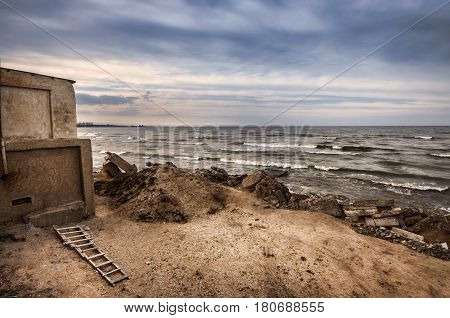 Beautiful Surreal Landscape Of Abandoned House And Ladder On Rocky Seashore At Sunset Time. Cloudy W