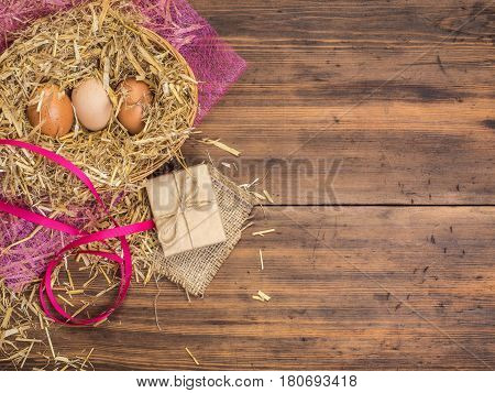Brown eggs in hay nest. Rural eco background with brown chicken eggs, red ribbon and straw on the background of old wooden planks. Top view. Creative background for Easter cards or restaurant menu
