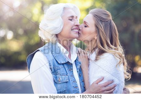 Exchanging endorphins . Positive amused happy woman enjoying walk in the park while expressing love and kissing aged mother