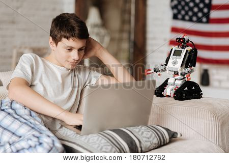 It is exiting. Little nice boy smiling while looking at computer watching something and getting pleasance