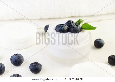 Skincare cream container with fresh indigo blueberries. White and blue tones. Holistic botanical beauty treatment product.