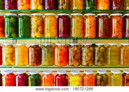 Various jars with Home Canning Fruits and Vegetables jam on glass shelves