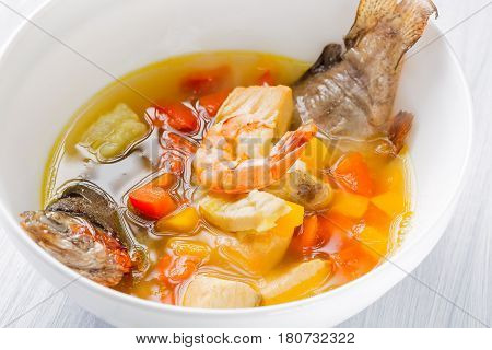 Fish soup with vegetables, shrimps and potatoes in white plate close up.