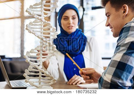 Involved in studying process. Pleasant delighted student studying with muslim girl and sitting at the table while getting ready for genetics classes