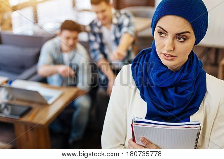 Gender inequality. Female muslim woman holding textbooks and standign in the cafe while being abused by her groupmates