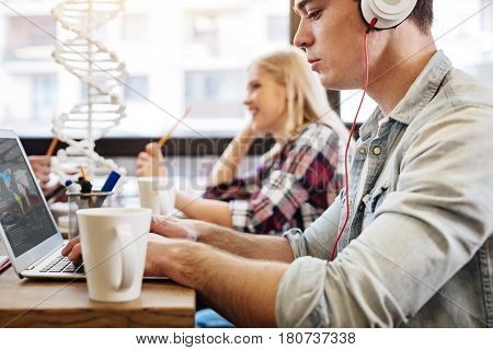 Online learning. Pleasant concentrated student using laptop and learning online while sitting in the cafe with his groupmates