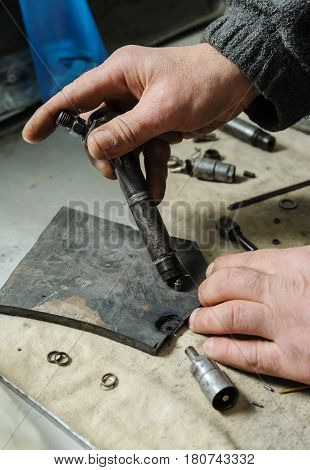 Mechanics repairing a diesel injector. Mans hands disassemble a injector to spare parts.